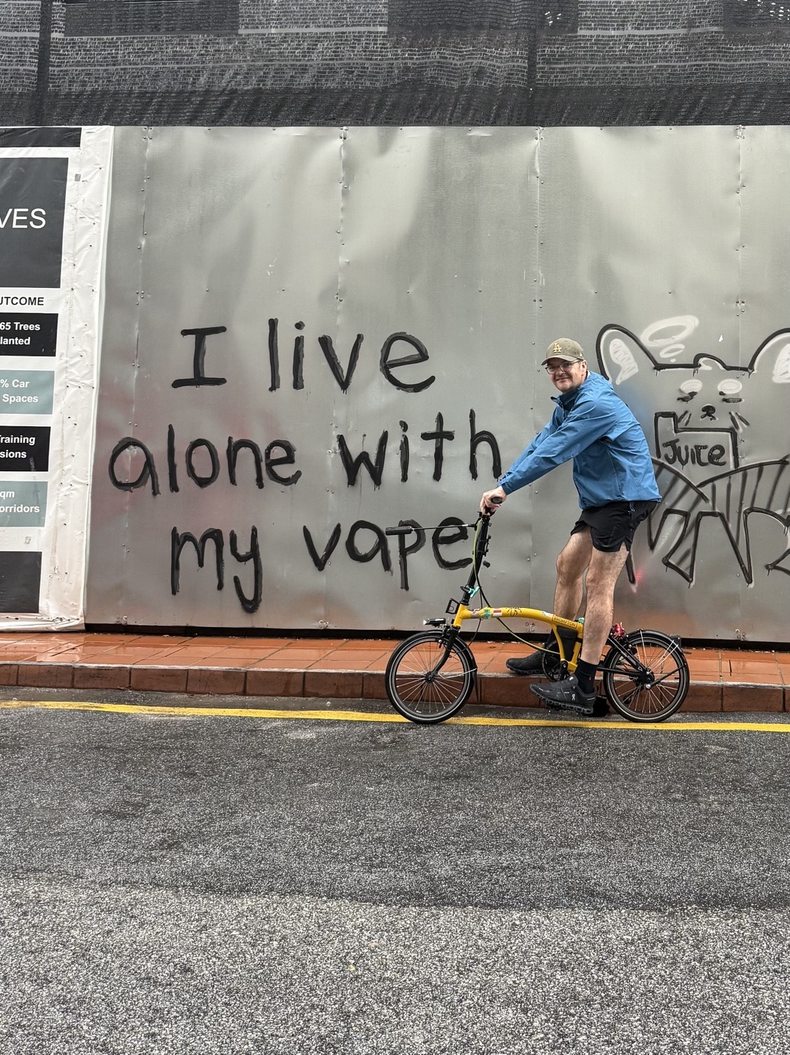 John sitting on his yellow Brompton bicycle in front of street art